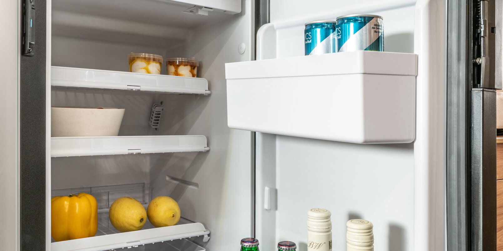 Open koelkast in de HYMER CamperVan gevuld met flessen en blikjes, citroenen, paprika's en andere boodschappen