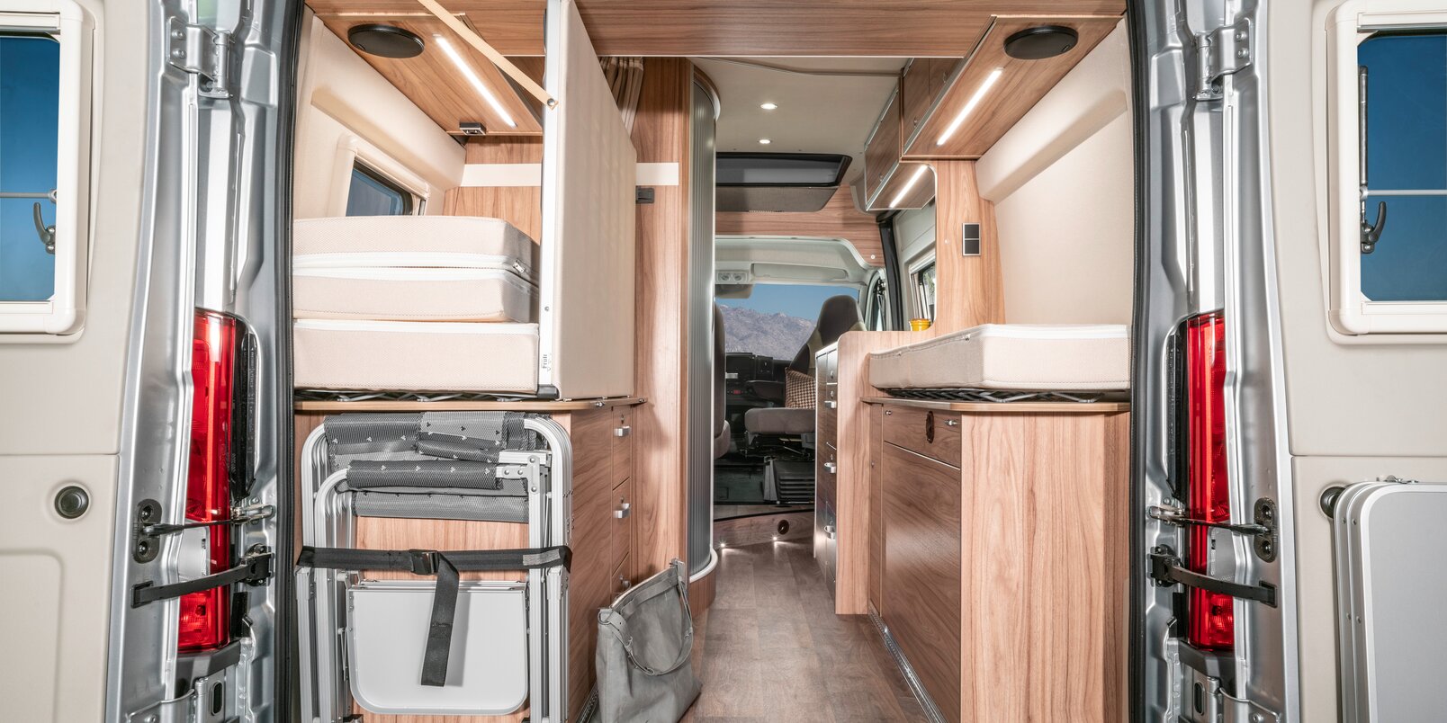 Open tailgate in the HYMER Camper Van with a view of the interior of the vehicle: bed area, mattresses, storage space, refrigerator, kitchen