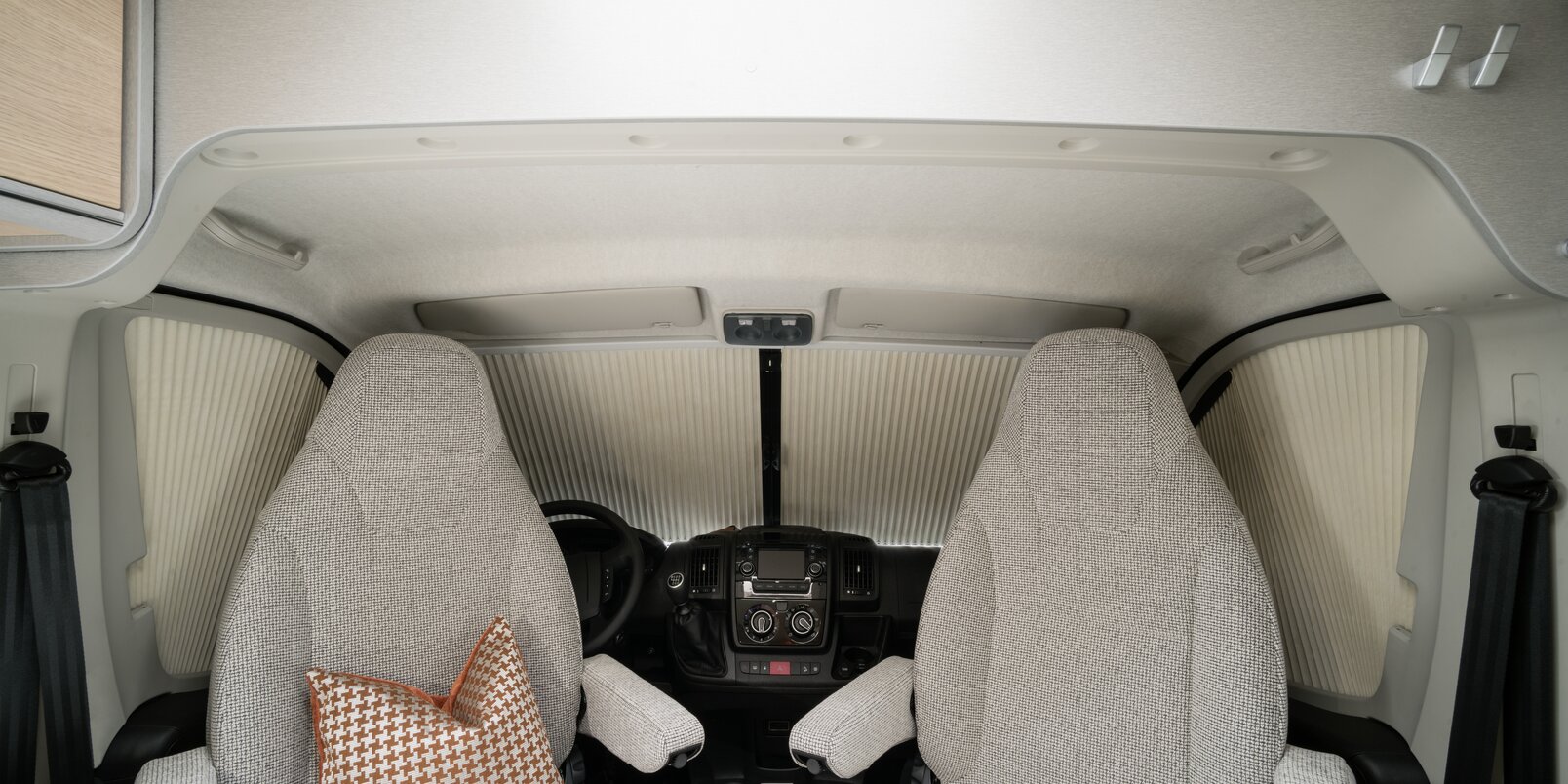 Fiat-bestuurderscabine met bestuurdersstoelen, sierkussens, dashboard en vouwgordijnsysteem in de HYMER-camper