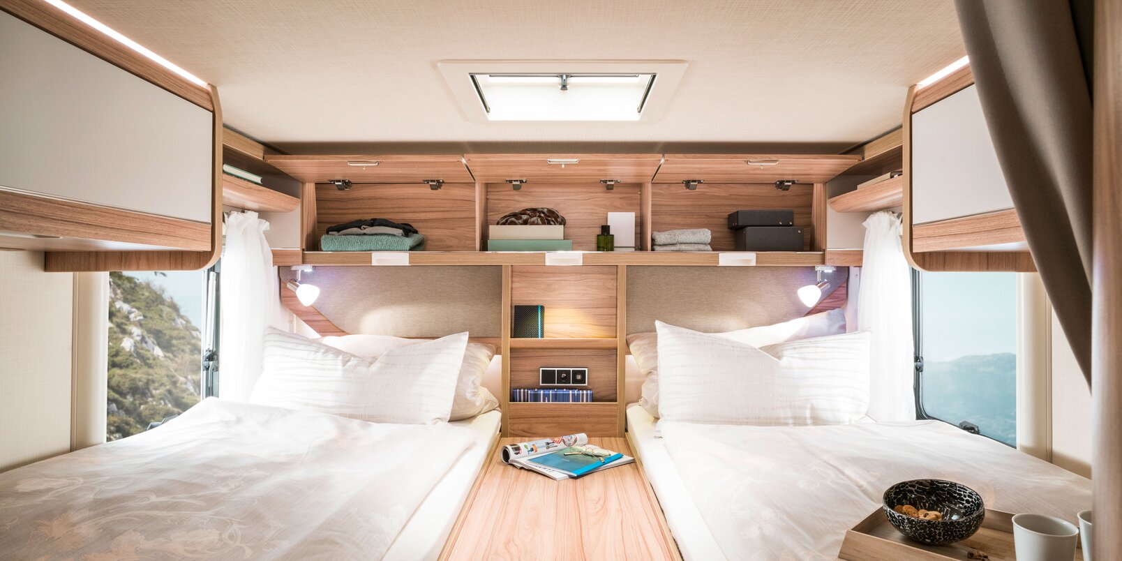 Schlafbereich im HYMER-Exsis i: Bezogene Längseinzelbetten, mittige Ablage, geöffnete und befüllte Dachstauschränke im Heck