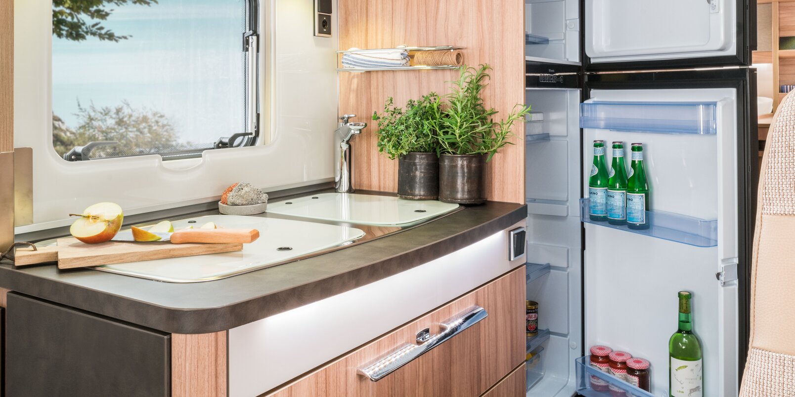 Küchenblock mit eingeklappter Arbeitsplattenerweiterung, offenen, vollen Dachstauschränken und Kühlschrank im HYMER Exsis-i