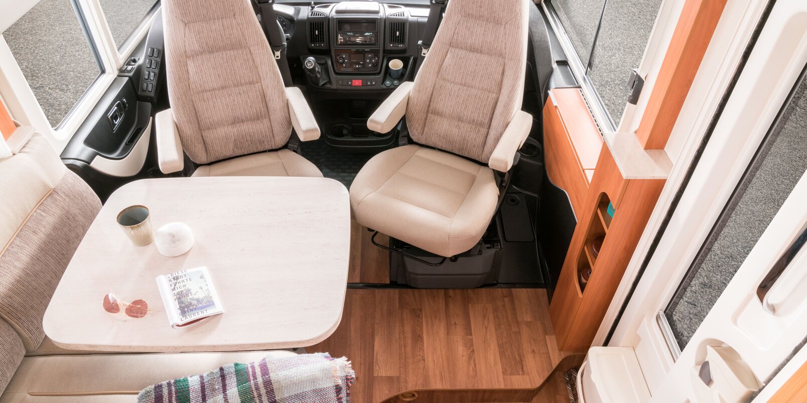 Living area in the HYMER Exsis i 504: driver's seats turned towards the seating group, set table, entrance door