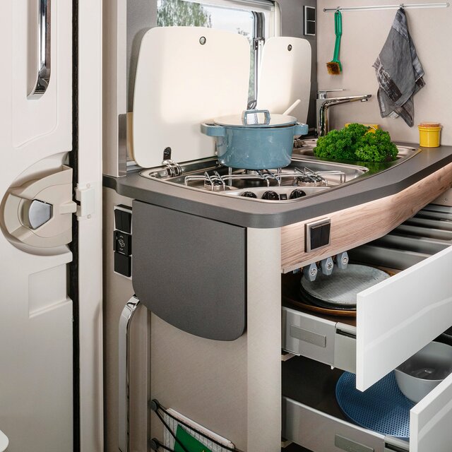 Opened drawers filled with dishes and a blue saucepan on the hob in the kitchen block of the HYMER Exsis 580