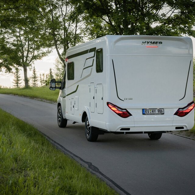 Side rear view of a semi-integrated HYMER motorhome travelling along a wooded road
