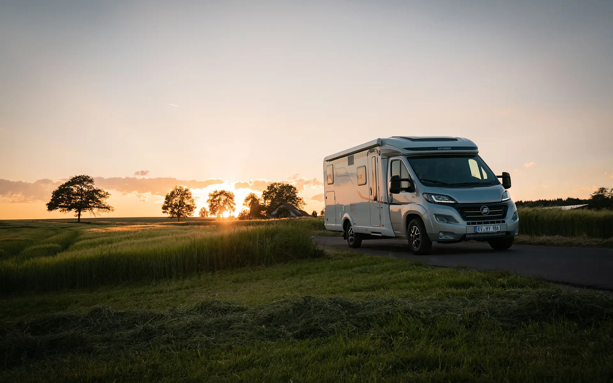 HYMER Exsis-t on a narrow street amid green meadows and cornfields at sunset