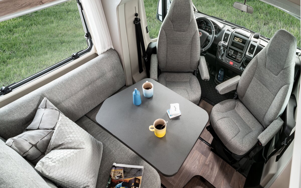 Seating group including driver's seats in the Exsis 580 with decorative cushions and magazine on the bench and dishes on the table