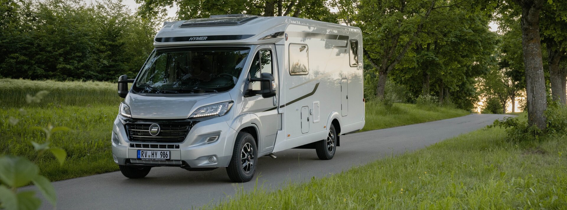 HYMER Exsis-t 580 on a narrow street amid trees and green meadows