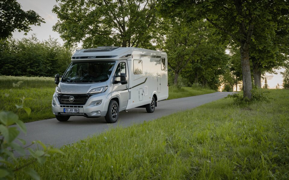 HYMER Exsis-t 580 auf einer schmalen Straße inmitten von Bäumen und grünen Wiesen
