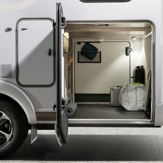 Opened garage door of an illuminated motorhome rear garage containing small luggage items
