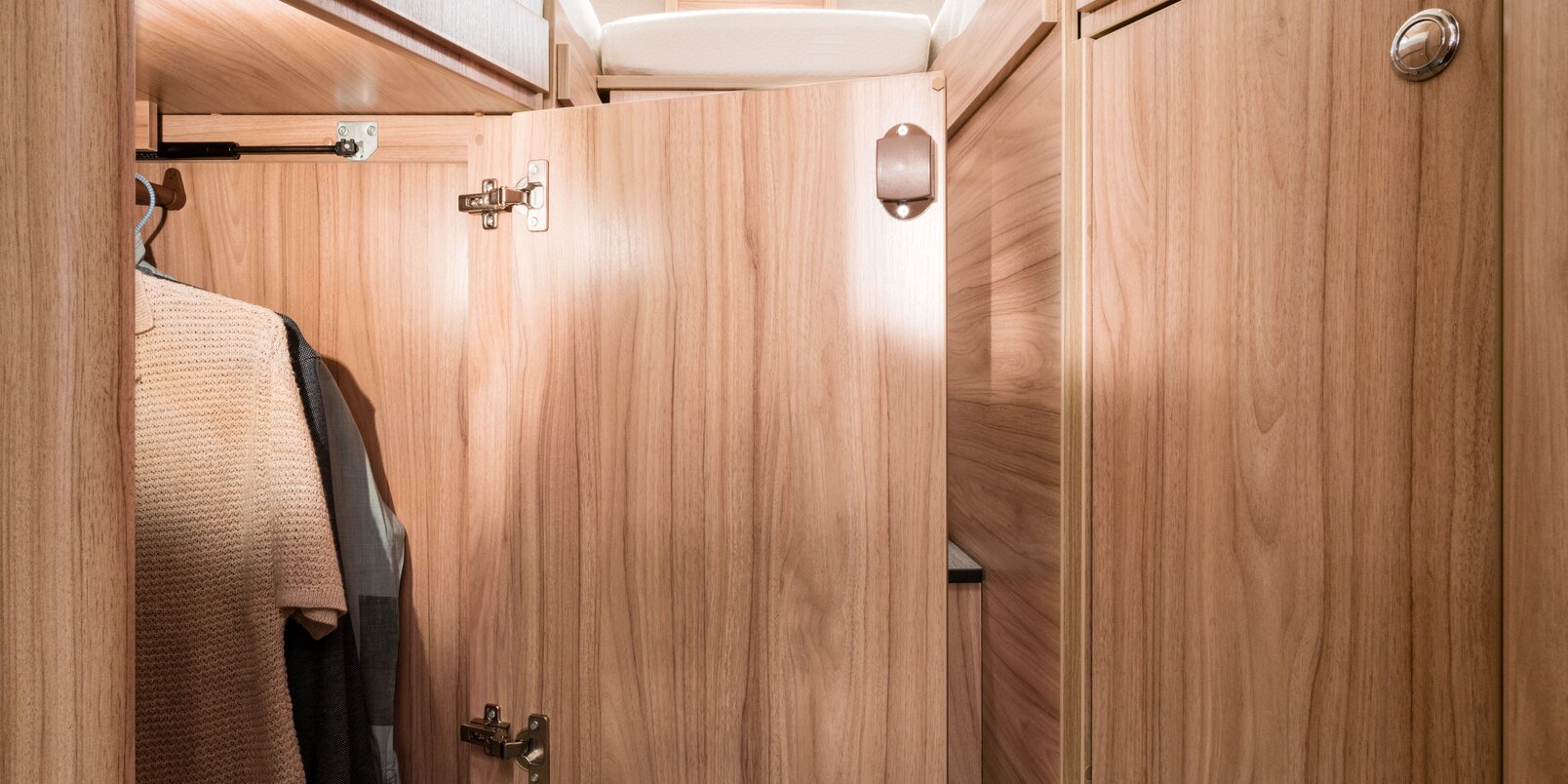 Open, illuminated wardrobe with hangers on the rail under the bed in the rear of the HYMER Exsis-t
