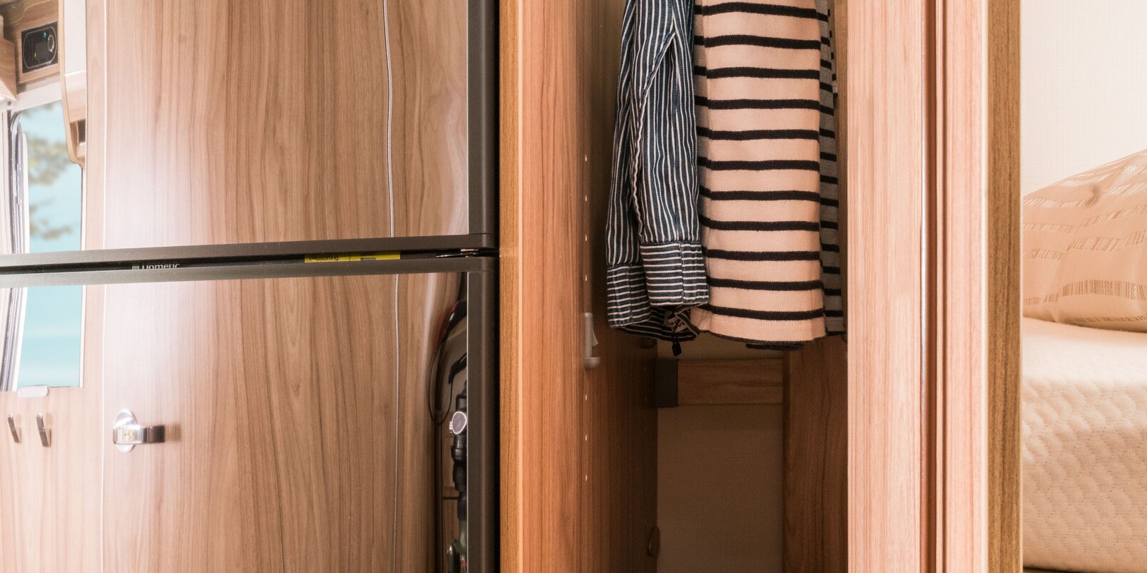 Hoher Kleiderschrank im Wohnmobil Exsis: mit Oberteilen behängte Stange und befülltes Ablagefach