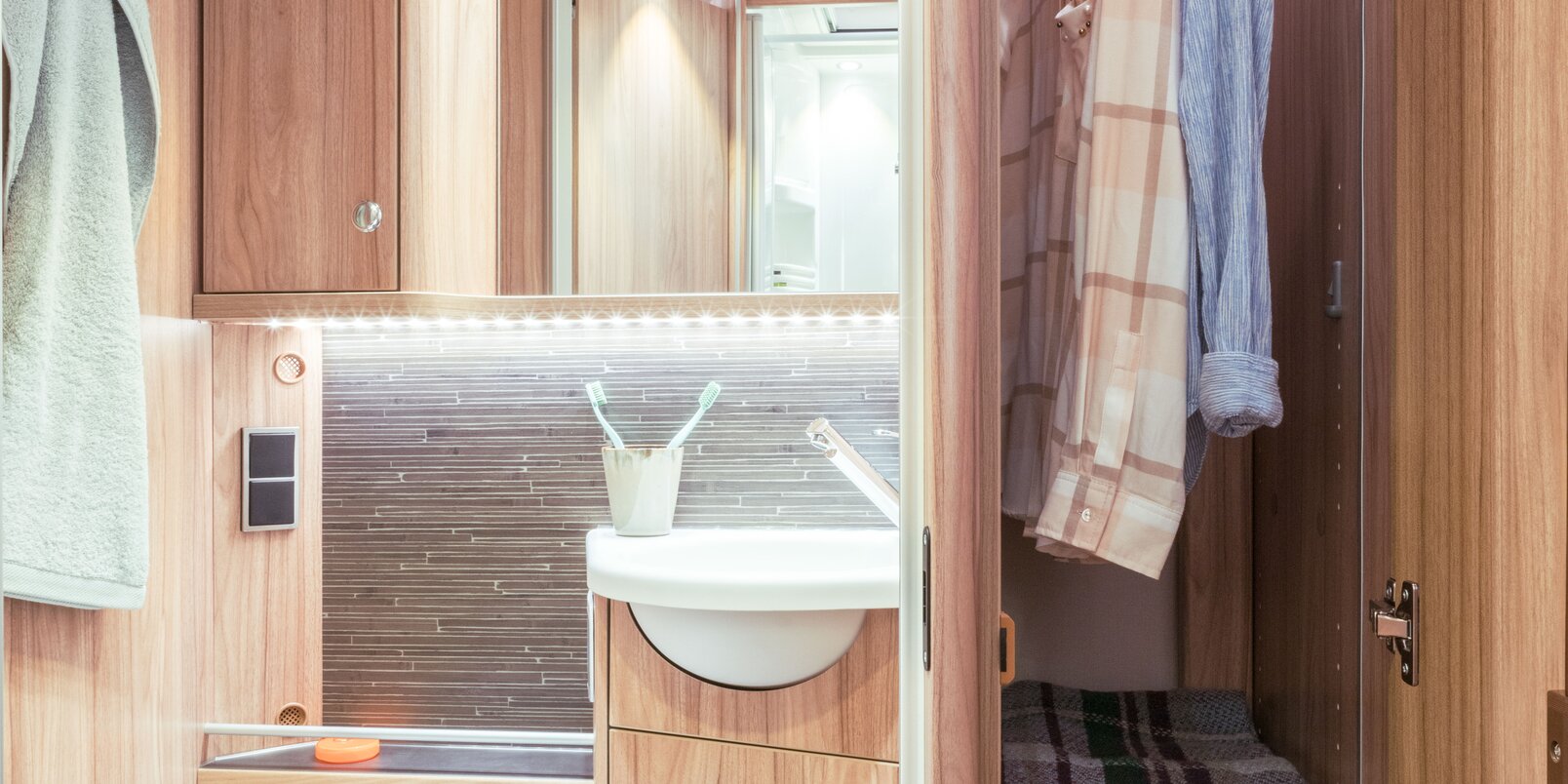 Bad im HYMER Exsis-t: Toilette, Waschbecken, Spiegel, Stauschränke, Dachfenster und daneben hoher, befüllter Kleiderschrank