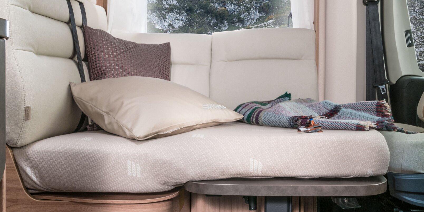 Zum Bett umgebaute Sitzgruppe mit Kissen und Decke im teilintegrierten Hymermobil Exsis-t 