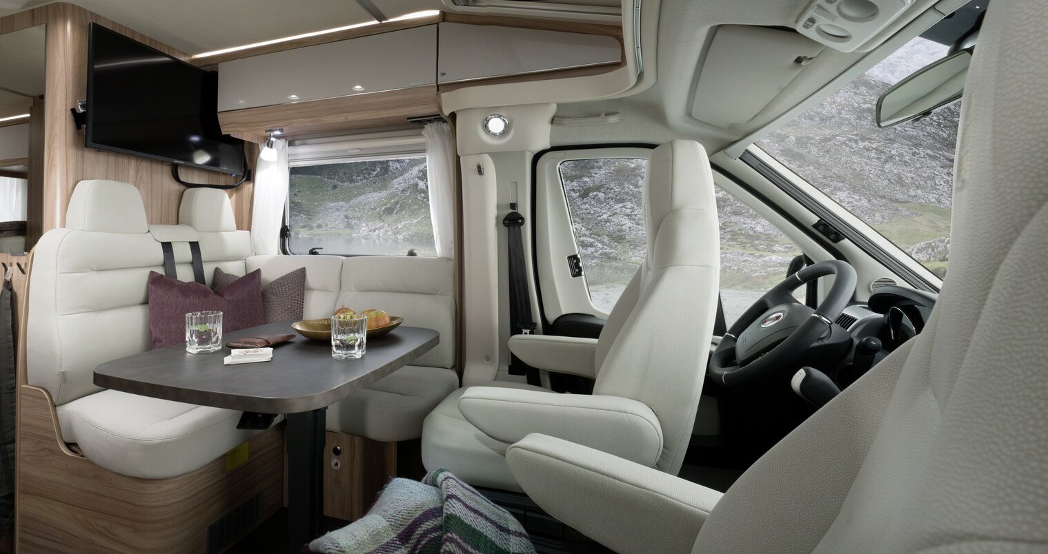 Lounge seating group including driver's seats in light upholstery with a set table, overhead storage cupboards and TV plasma in the HYMER Exsis-t