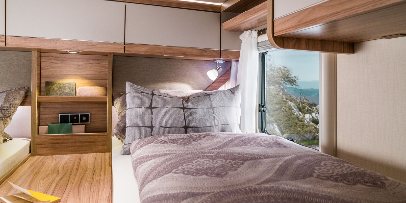 Covered lengthways single bed, central shelf with utensils, overhead storage cupboards and reading lamp in the HYMER Exsis-t