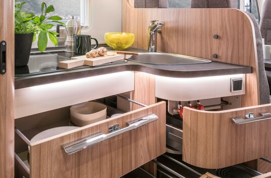 Open drawers in the kitchen block filled with kitchenware, cutting board and herb pot on shelf in the HYMER Exsis-t