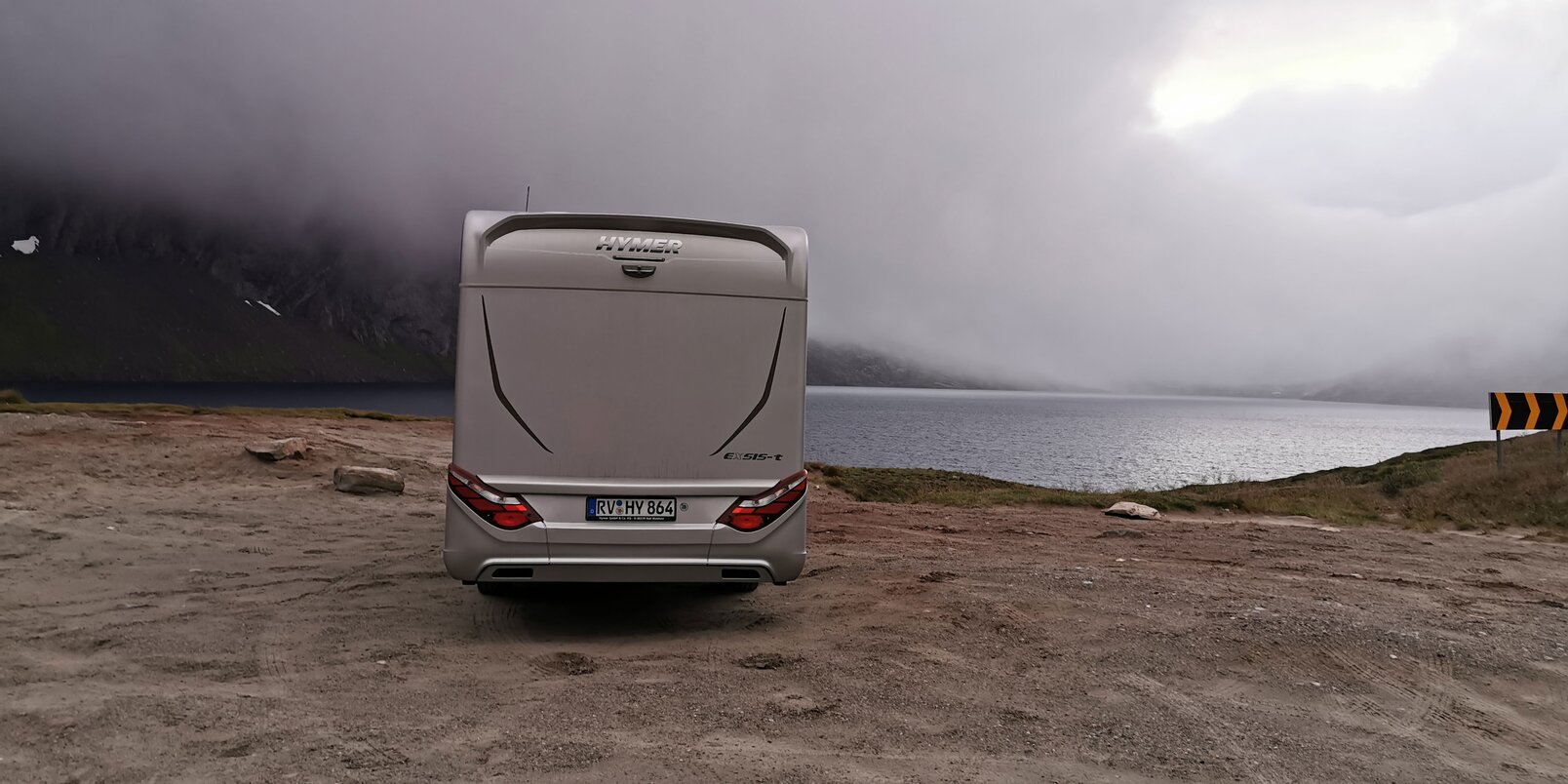 Reisemobil HYMER Exsis-t von hinten am kiesigen Ufer in einem wolkenverhangenen Fjord