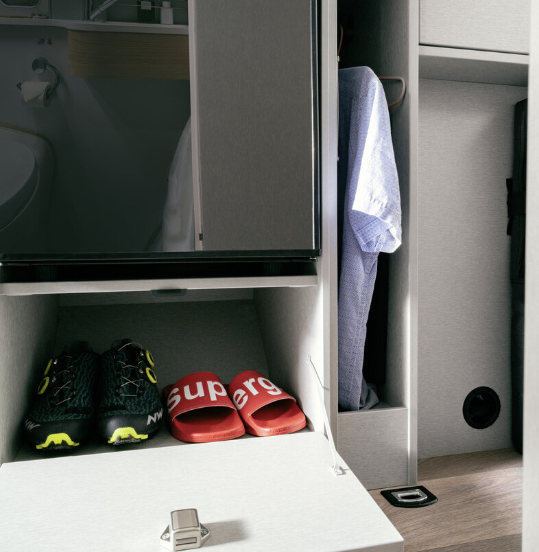Compartimentos con zapatos debajo del frigorífico y compartimento de almacenamiento con barra para colgar ropa en el HYMER Free S