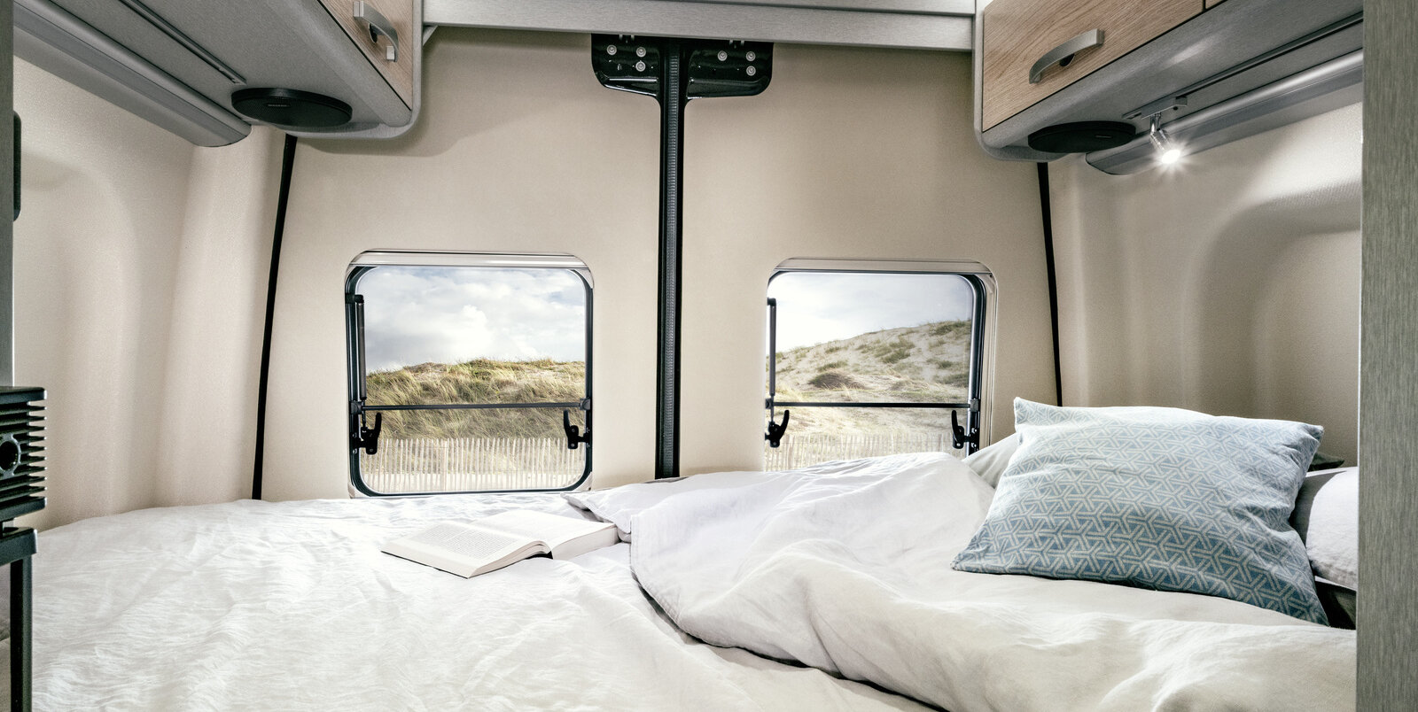 Cama con funda con almohadas y armarios abiertos para libros y almacenamiento en la parte trasera del HYMER Camper Van Free S