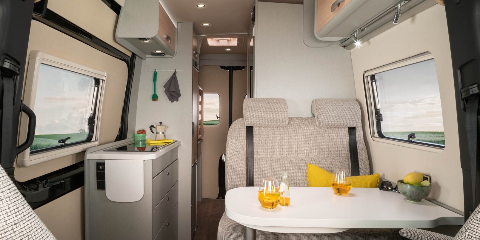 HYMER Camper Van Free S 600 ohjaamon istuimet, pöytä, keltainen tyyny, tavaraa pöydällä ja keittiö