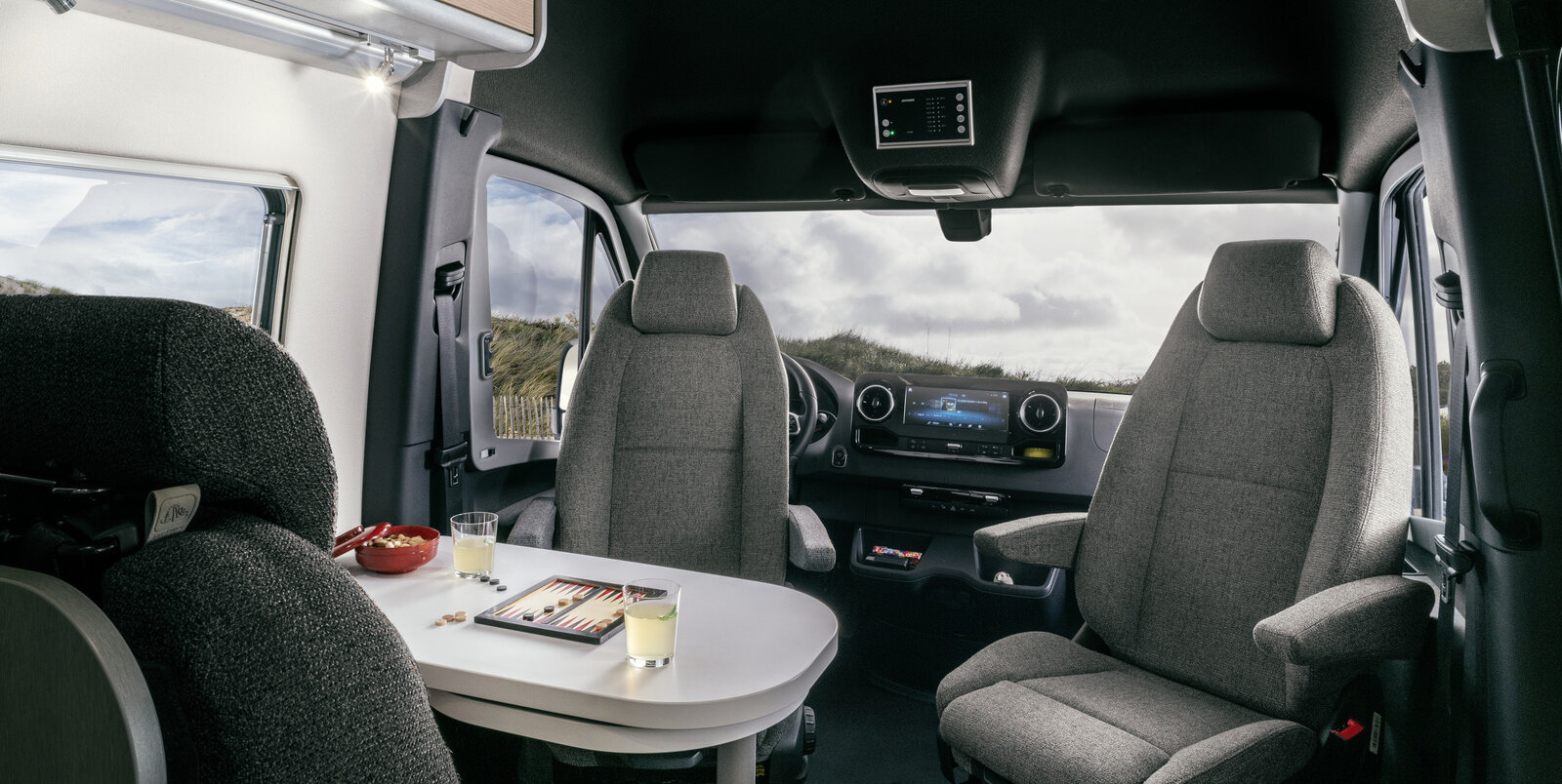 Zitgroep met bestuurdersstoelen, tafel, keukengerei op tafel en dashboard in de HYMER Free S 600