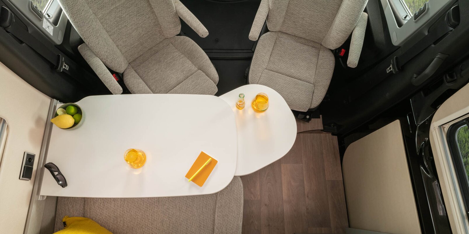 Seating group with driver's seats and table, yellow cushions and utensils on the table in the HYMER Camper Van Free S.