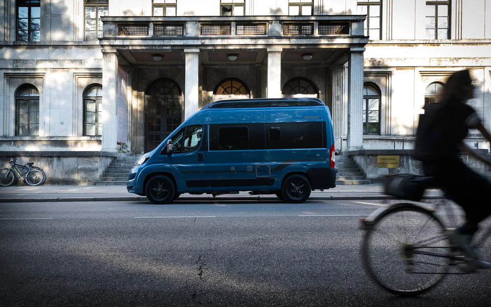 Blau-metallic lackierter Camper Van HYMER Free parkt vor altem Gebäude in der Stadt