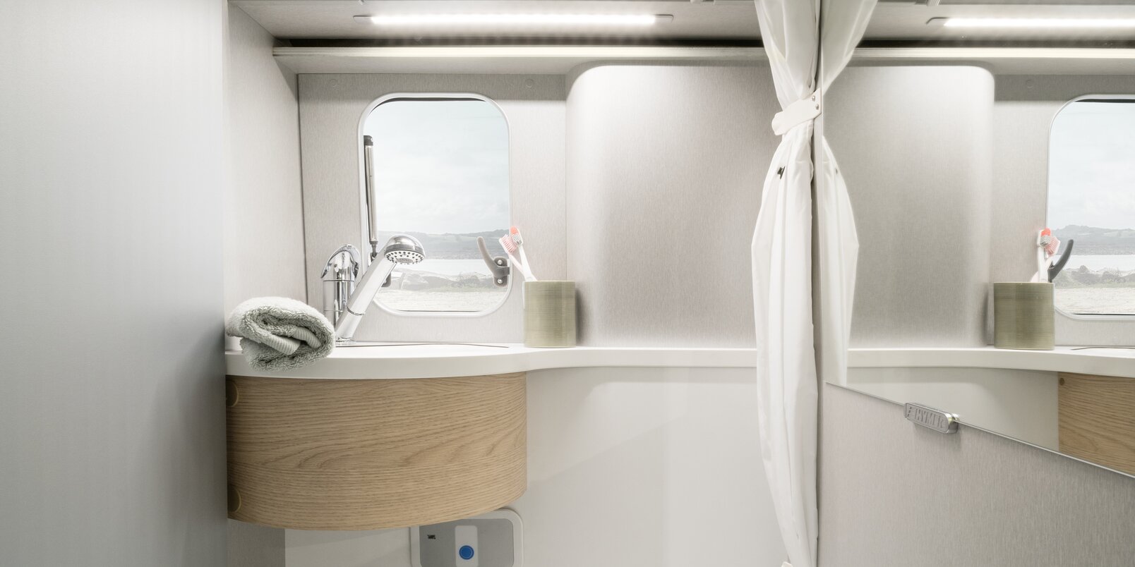Toilette, Waschbecken, offener Spiegelschrank, Duschvorhang, Ablagefach und Fenster im Kompaktbad beim HYMER Free
