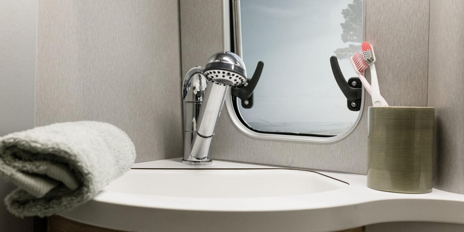 Waschbecken mit Duscharmatur, Handtuch, Zahnputzbecher mit zwei Bürsten und Fenster im Bad des HYMER Free