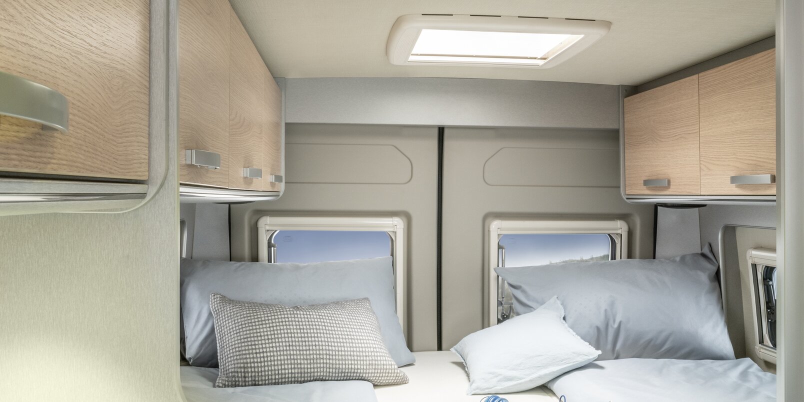 Mit Betten bezogene Liegefläche, Decke, Zeitschrift, Kopfhörer und Dachstauschränke im Heck des HYMER Free 602