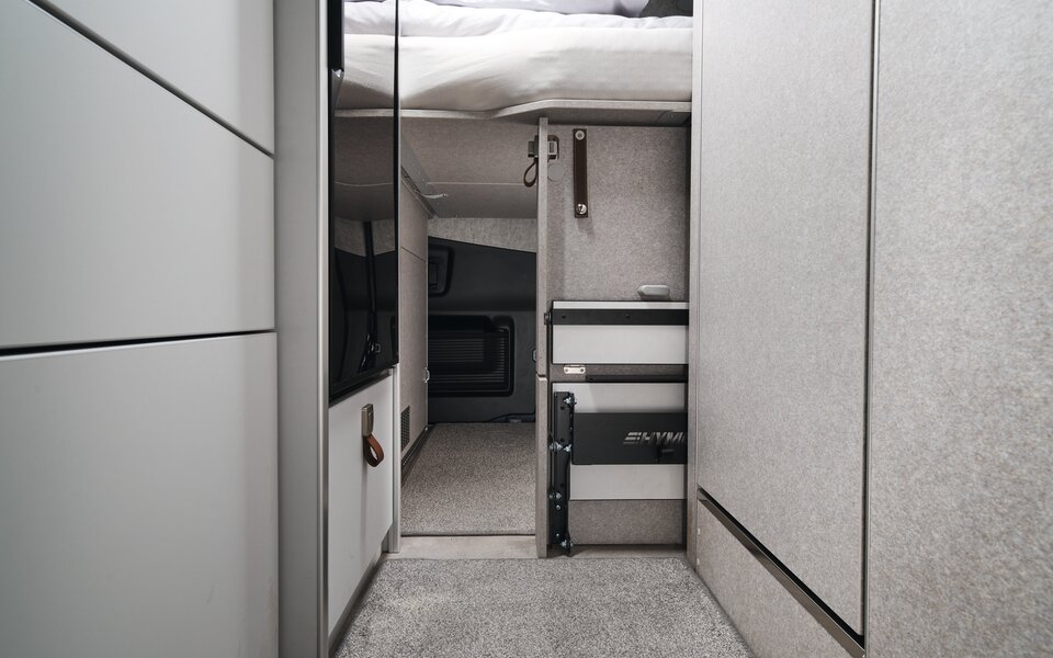 On peut voir que la garage arrière du HYMER Grand Canyon S dans le monde du style Pearl Grey est accessible depuis l'intérieur du véhicule sous le lit.