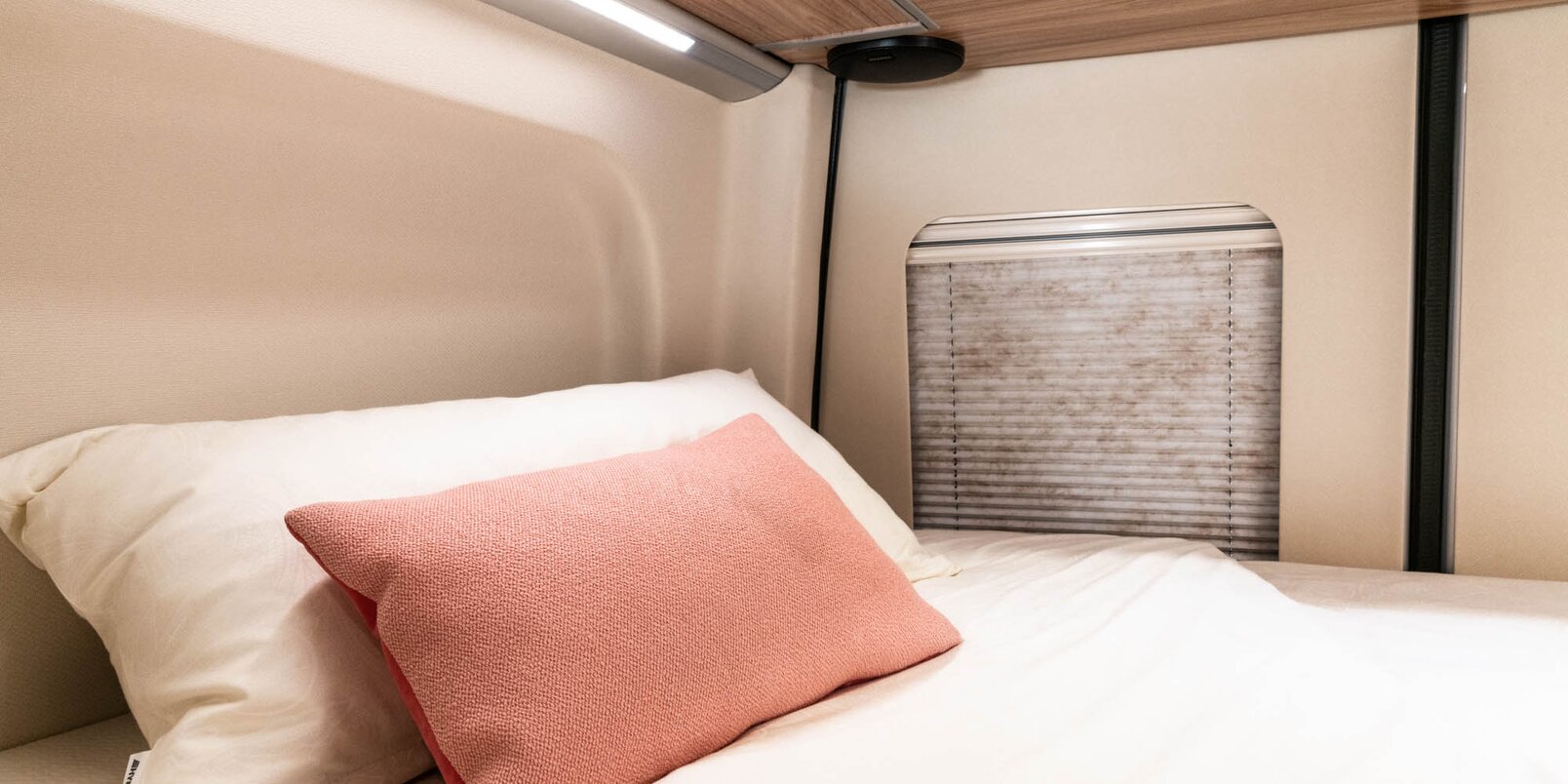 Rear bed covered with bed linen, pink decorative pillows, window with Roman shade on the HYMER Grand Canyon S