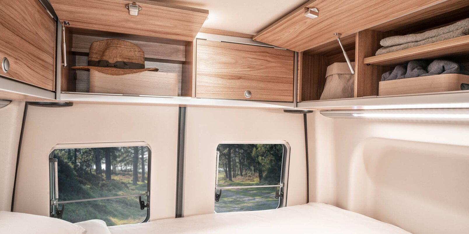 Made-up bed, newspaper, partly open overhead lockers filled with textiles and rear doors in the HYMER Grand Canyon S