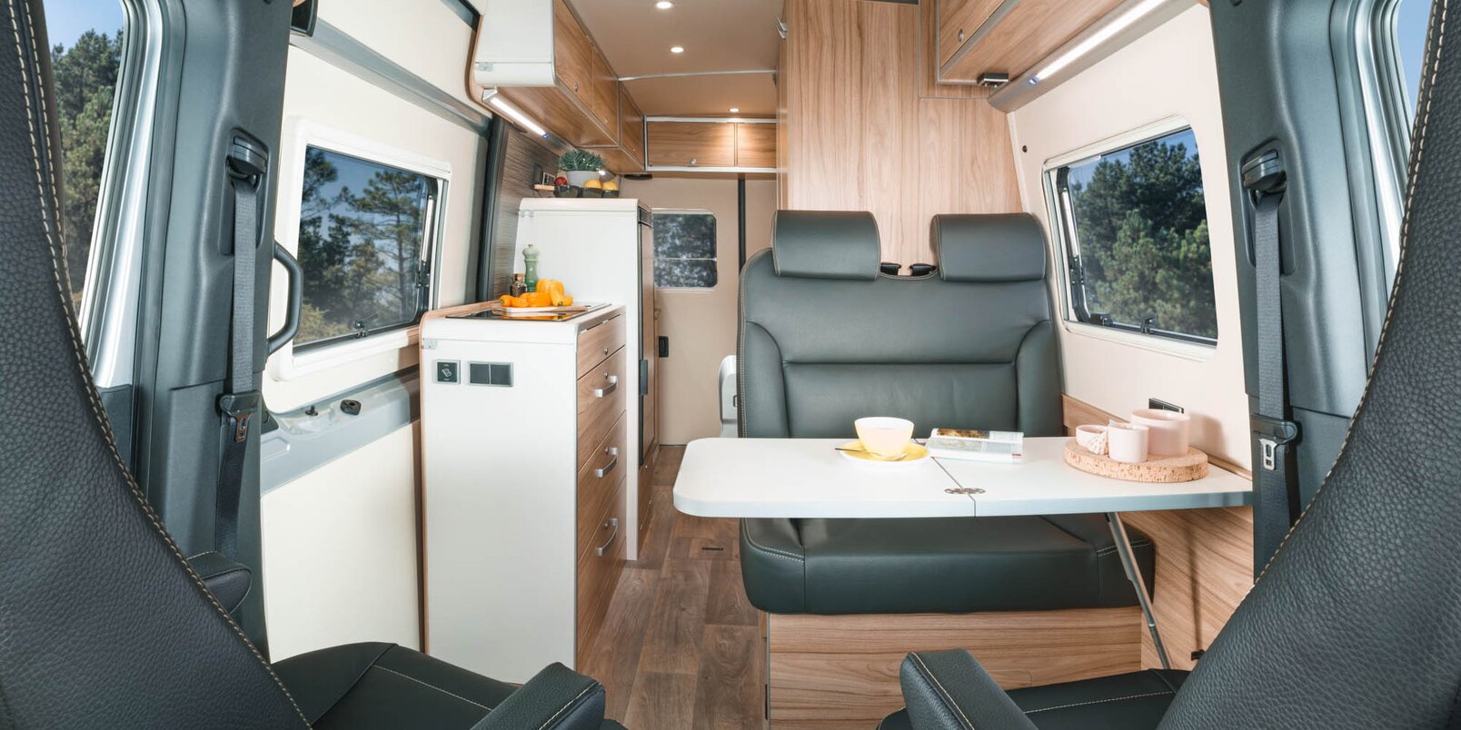 Sala de estar en el HYMER Grand Canyon S con asientos del conductor, zona de estar, mesa, bloque de cocina, zona trasera