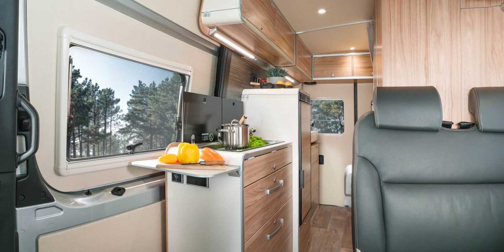 Bench, kitchen block with additional shelf, overhead storage cupboard, refrigerator, entrance door in the Mercedes-Sprinter HYMER Grand Canyon S