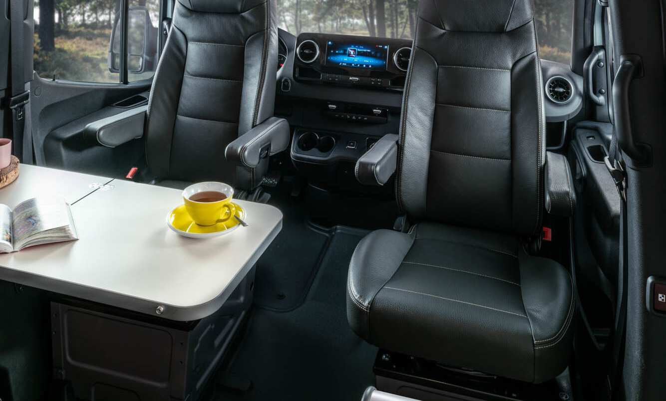 Table with yellow cup, driver and front passenger seats and the driver's cab in the HYMER Grand Canyon S