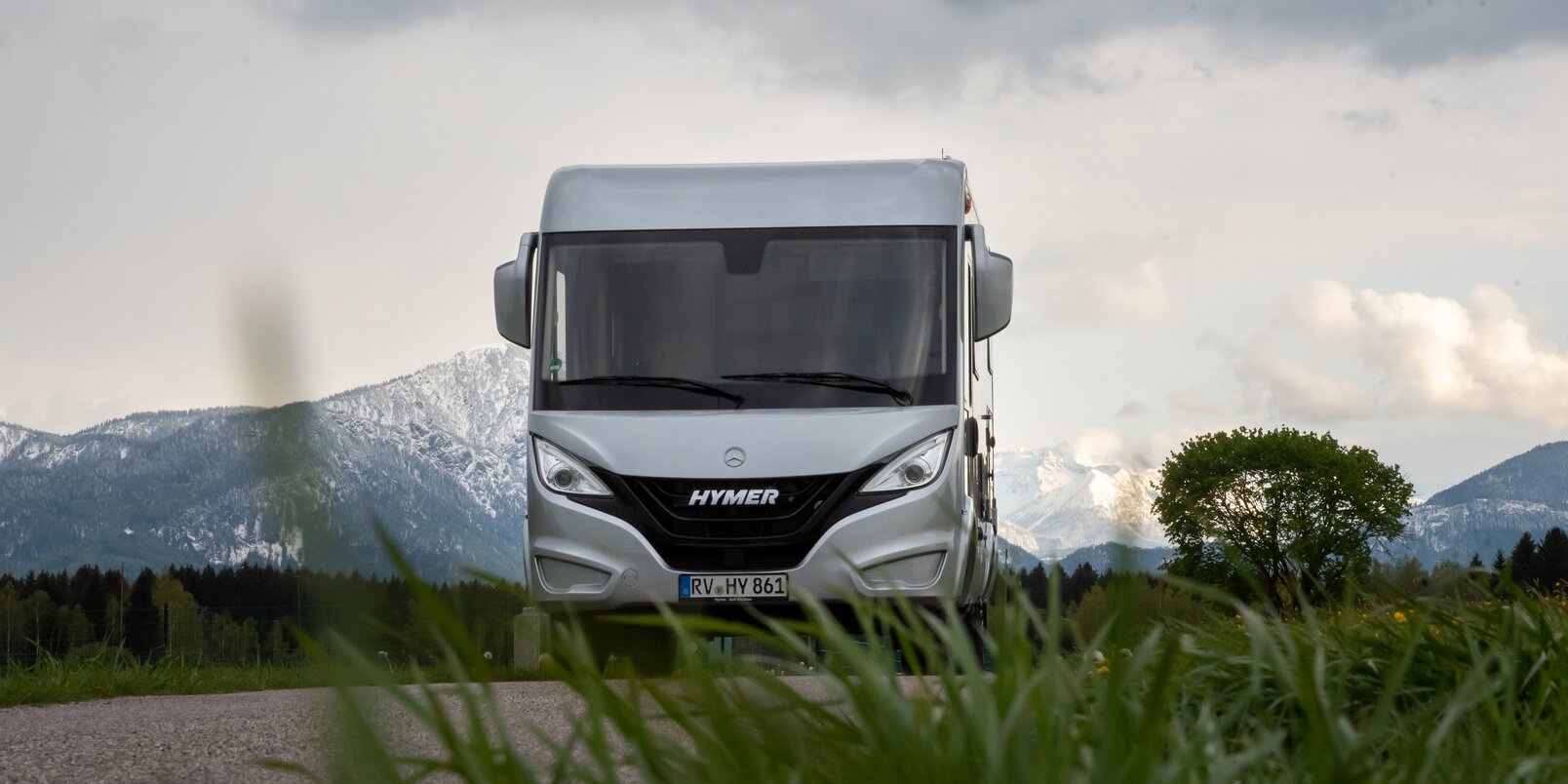 HYMER B ModernComfort in a meadow with a snow-covered mountain panorama and trees