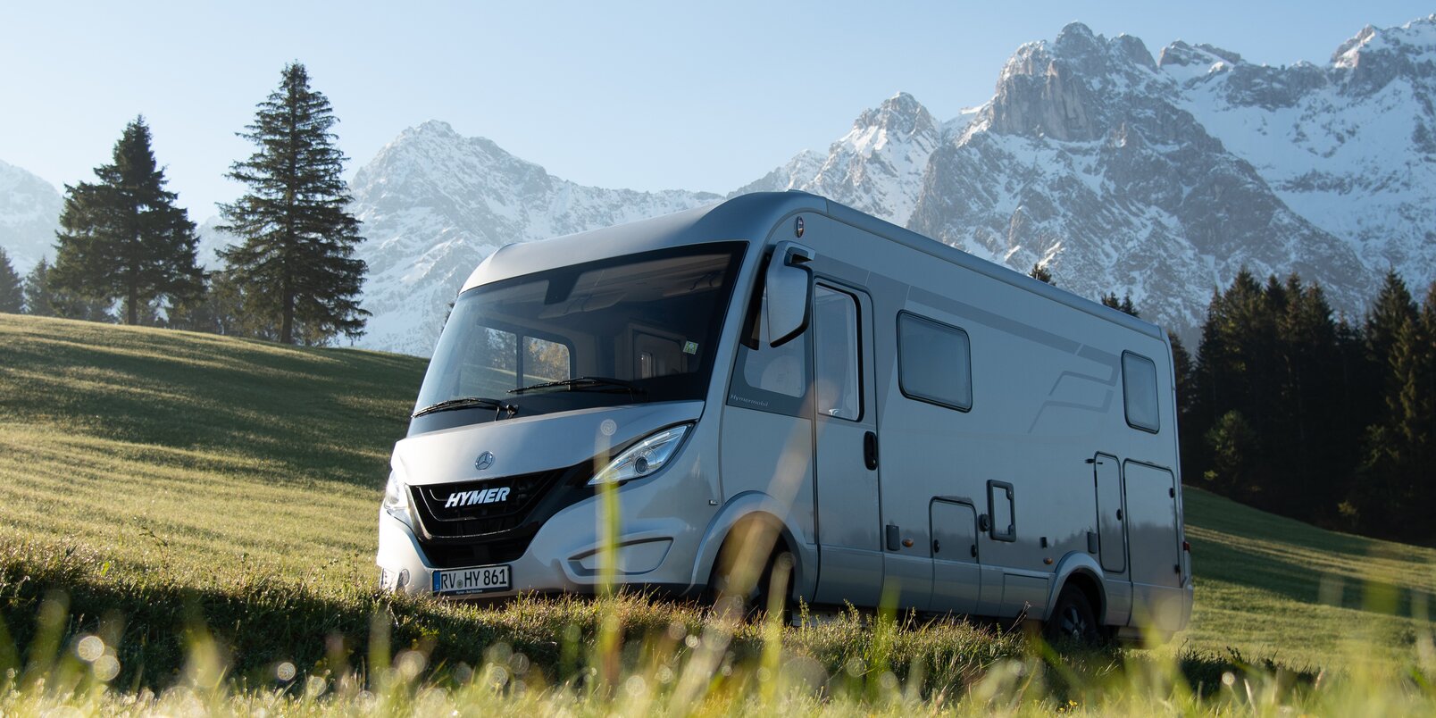 HYMER B ModernComfort in a meadow with snow-capped mountains and blue sky