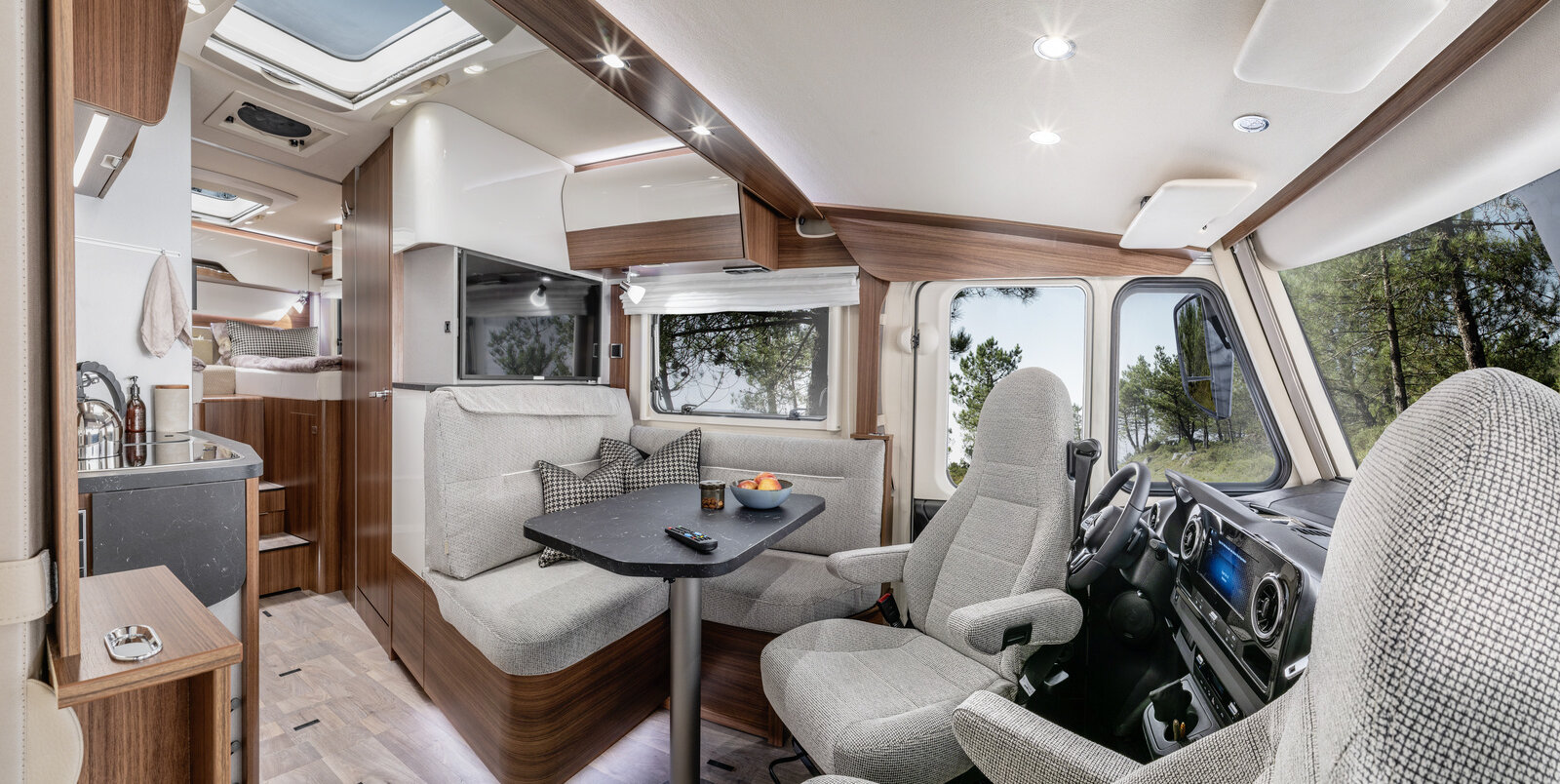 Lounge seating group with driver's seats and decorative cushions, TV plasma and kitchen in the HYMER B ModernComfort