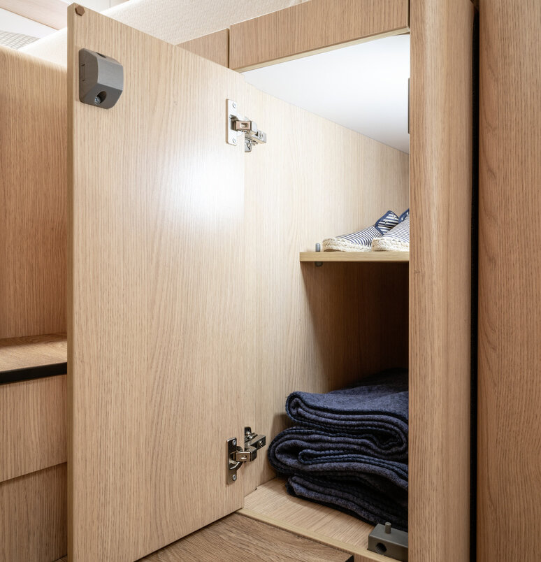 Open, illuminated wardrobe with shelves filled with shoes and towels under the rear bed of the B-MC I