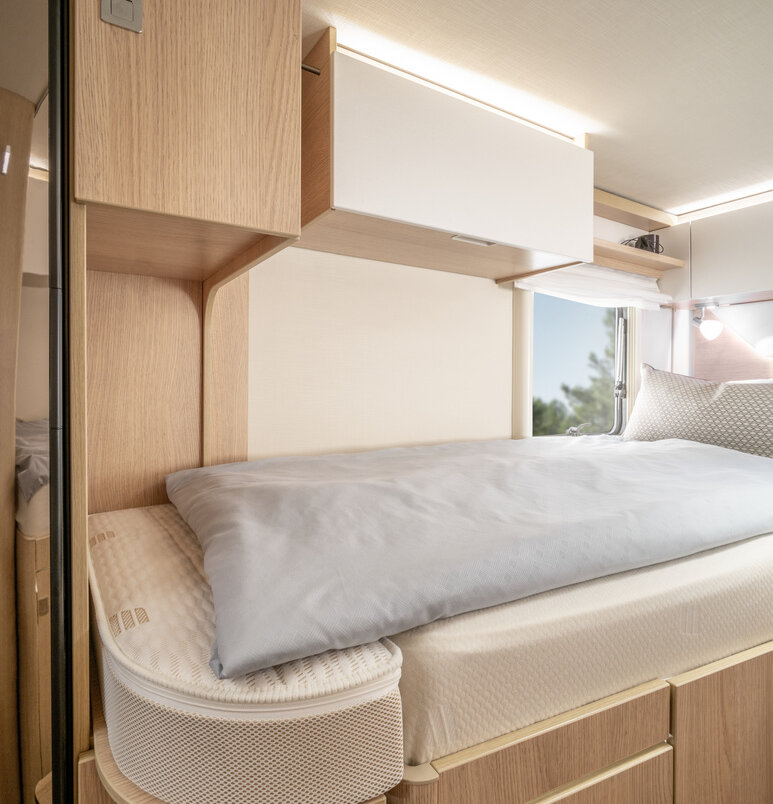 Lengthways single bed on the left with bed linen and overhead storage cupboard and cupboard under the bed in the HYMER B ModernComfort