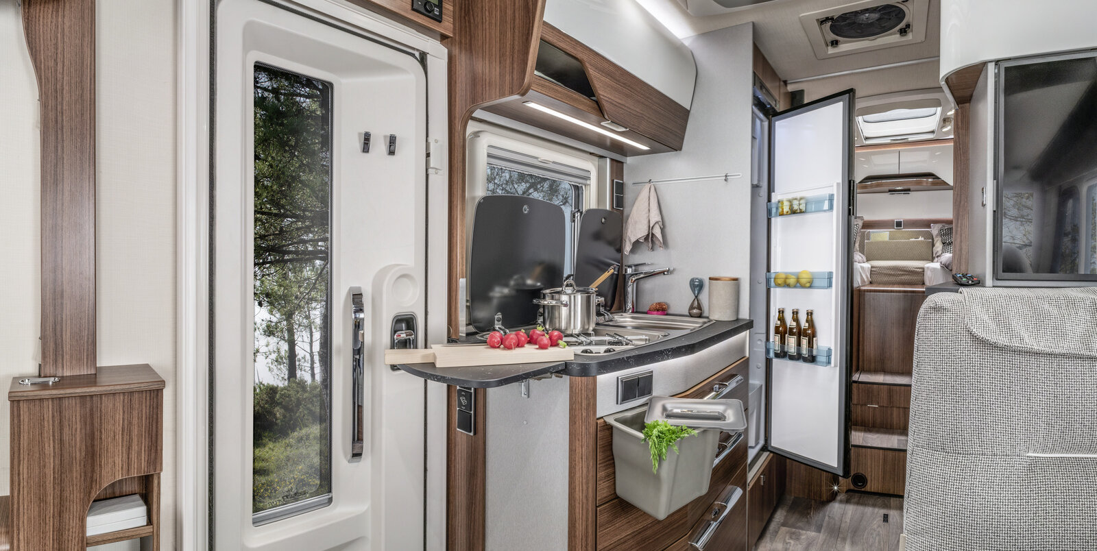 Cucina accanto alla porta d’ingresso, estensione piano di lavoro della cucina, pattumiera sul cassetto estraibile, frigorifero aperto nell’HYMER B-MC