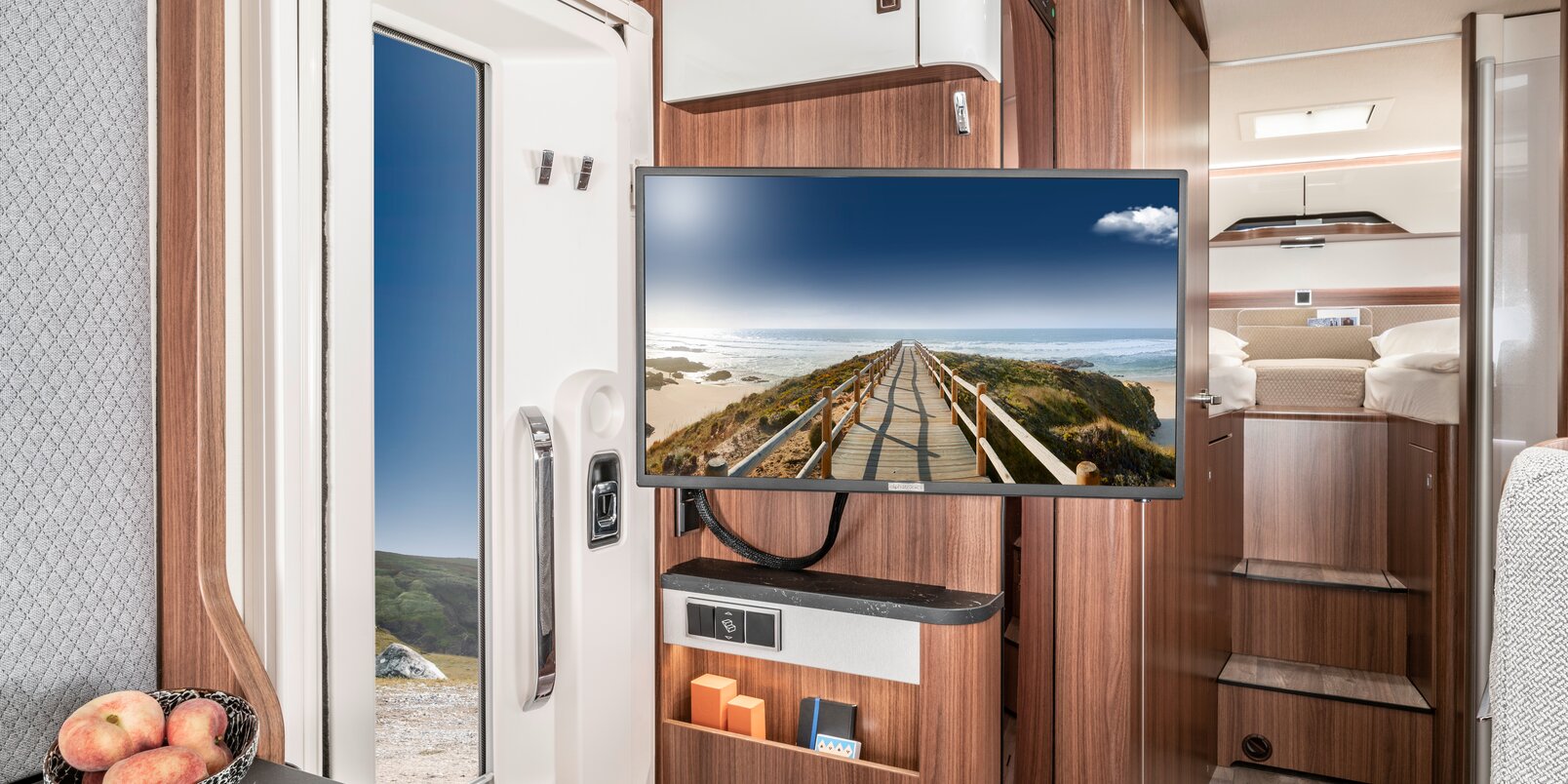 TV plasma with a still image from the beach with a wooden walkway next to the living room entrance door in the HYMER B Modern Comfort