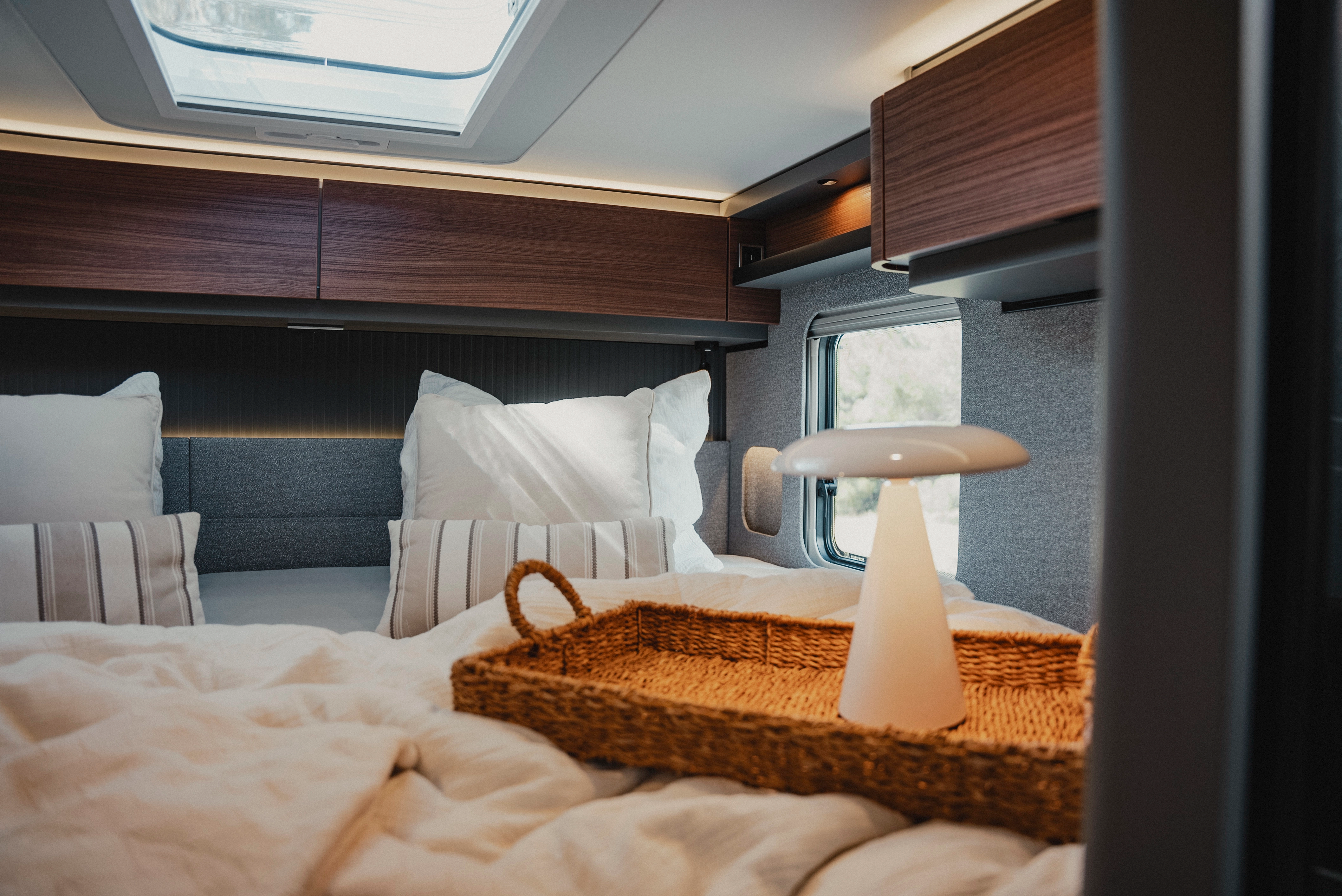 Ervaar luxueus comfort met een stijlvol ingerichte slaapruimte, aangevuld met moderne bovenkasten in houtafwerking, hier in Rochefort noten. De combinatie van natuurlijk licht en warme verlichting creëert een sfeer van ontspanning en elegantie voor uw reizen.