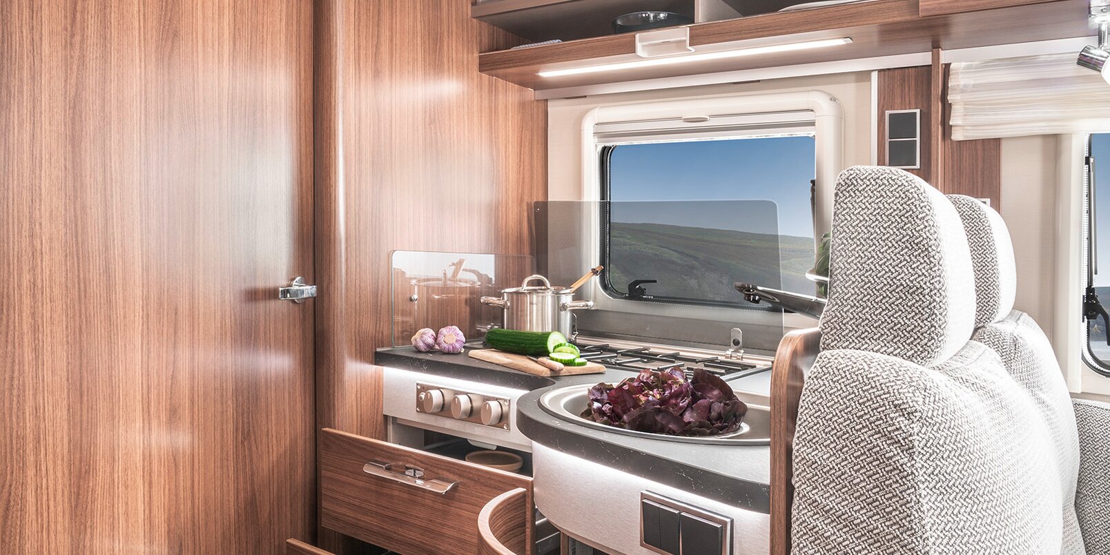 Open drawers / overhead storage cupboards in the kitchen full of kitchen utensils, rear wall cushions with headrests in the HYMER B-MC