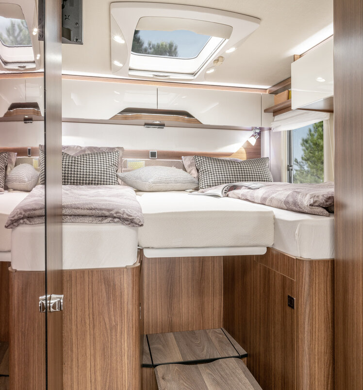 Mit Bettwäsche bezogene Einzelbetten und mittiges Zusatzpolster sowie ausklappbarer Tritt im Heckbereich des B ModernComfort