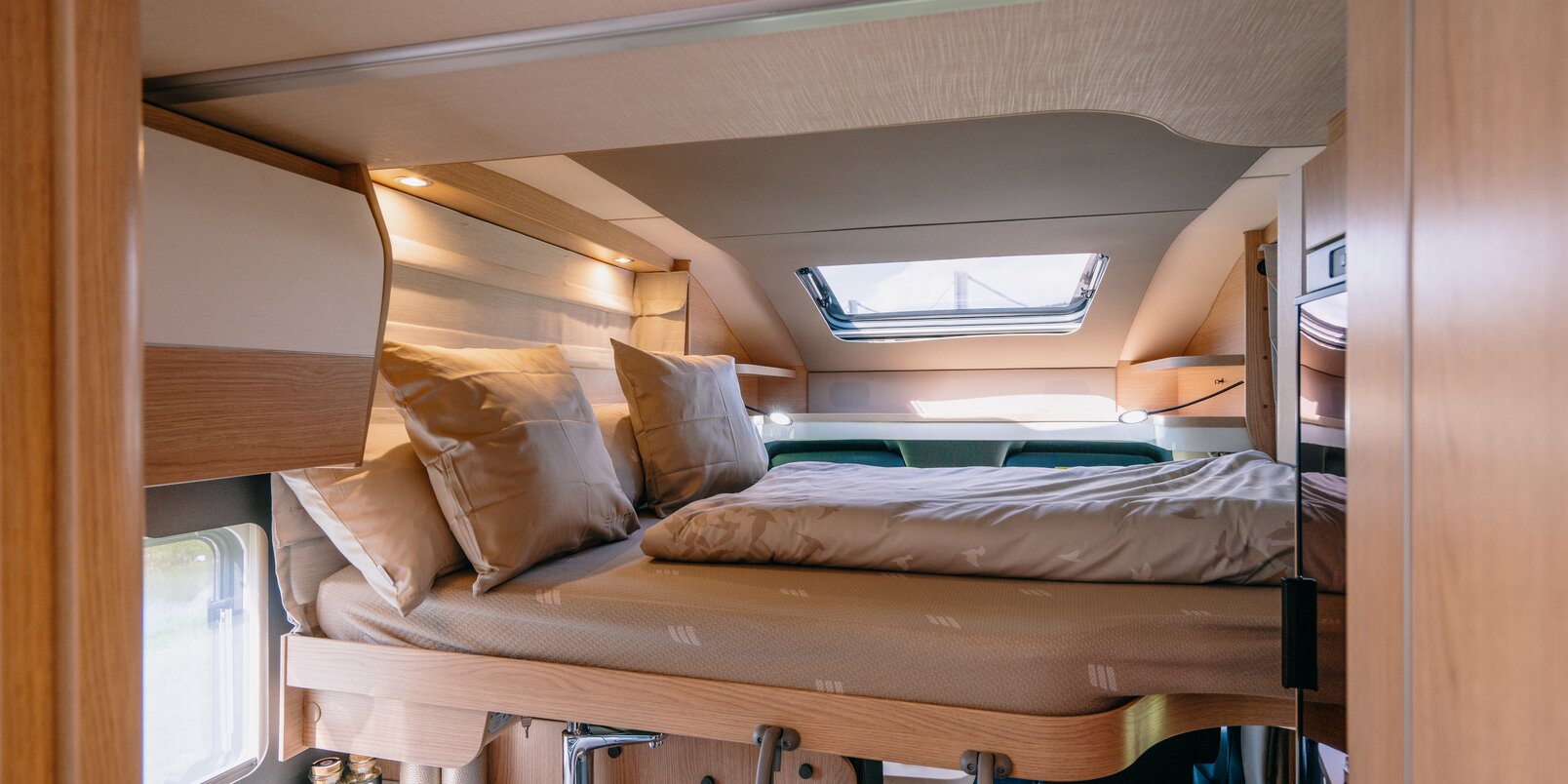 Lowered pull-down bed covered with bed linen above the seating area, access ladder on the HYMER B-MC T