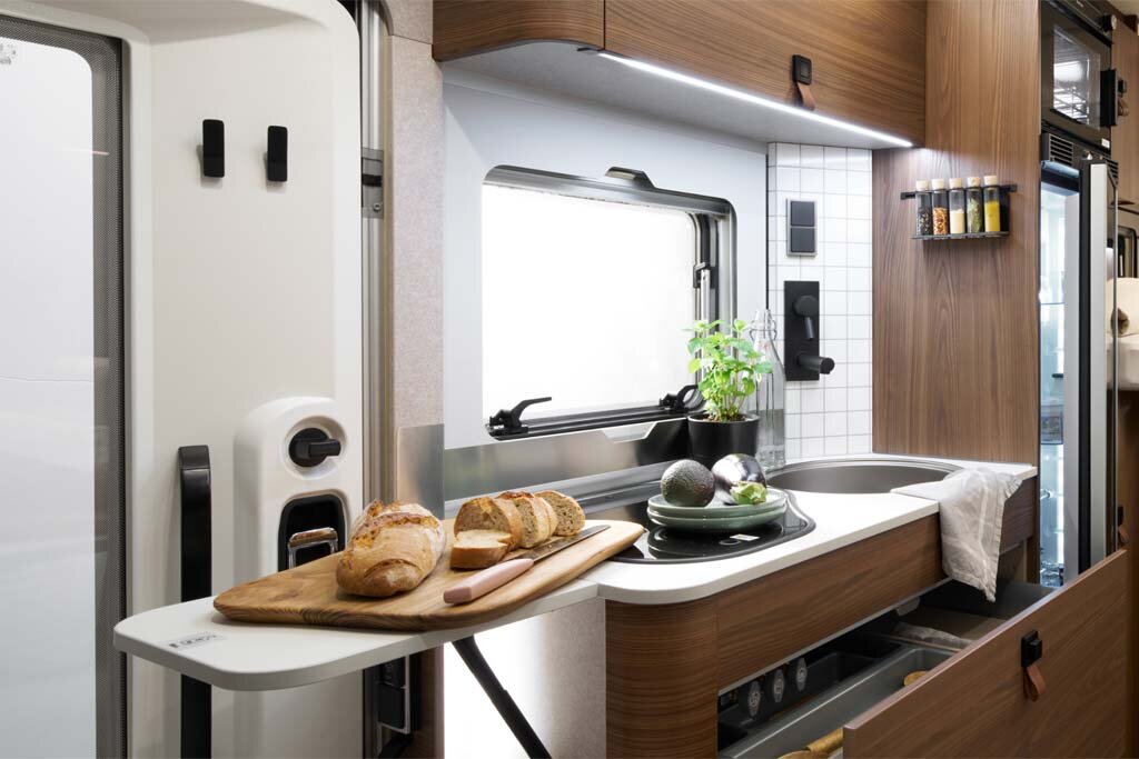 Auf der Küchenerweiterung im HYMER ML-T in der Stilwelt Velvet Ash liegt Brot. Im Hintergrund sind die gesamte Küchenzeile und das Fenster zu sehen.