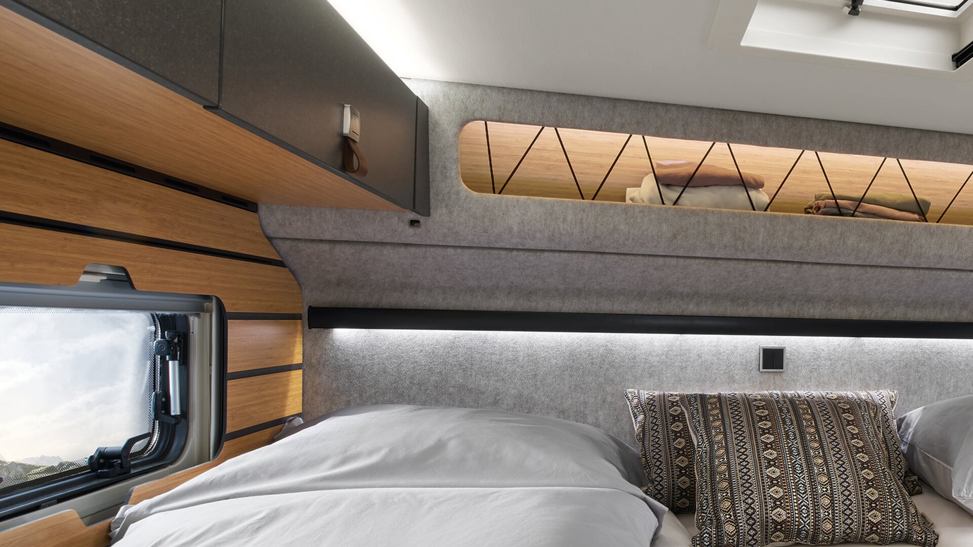 Rund um das Bett im HYMER ML-T in der Stilwelt Native Bamboo sind Dachstauschränke angebracht.