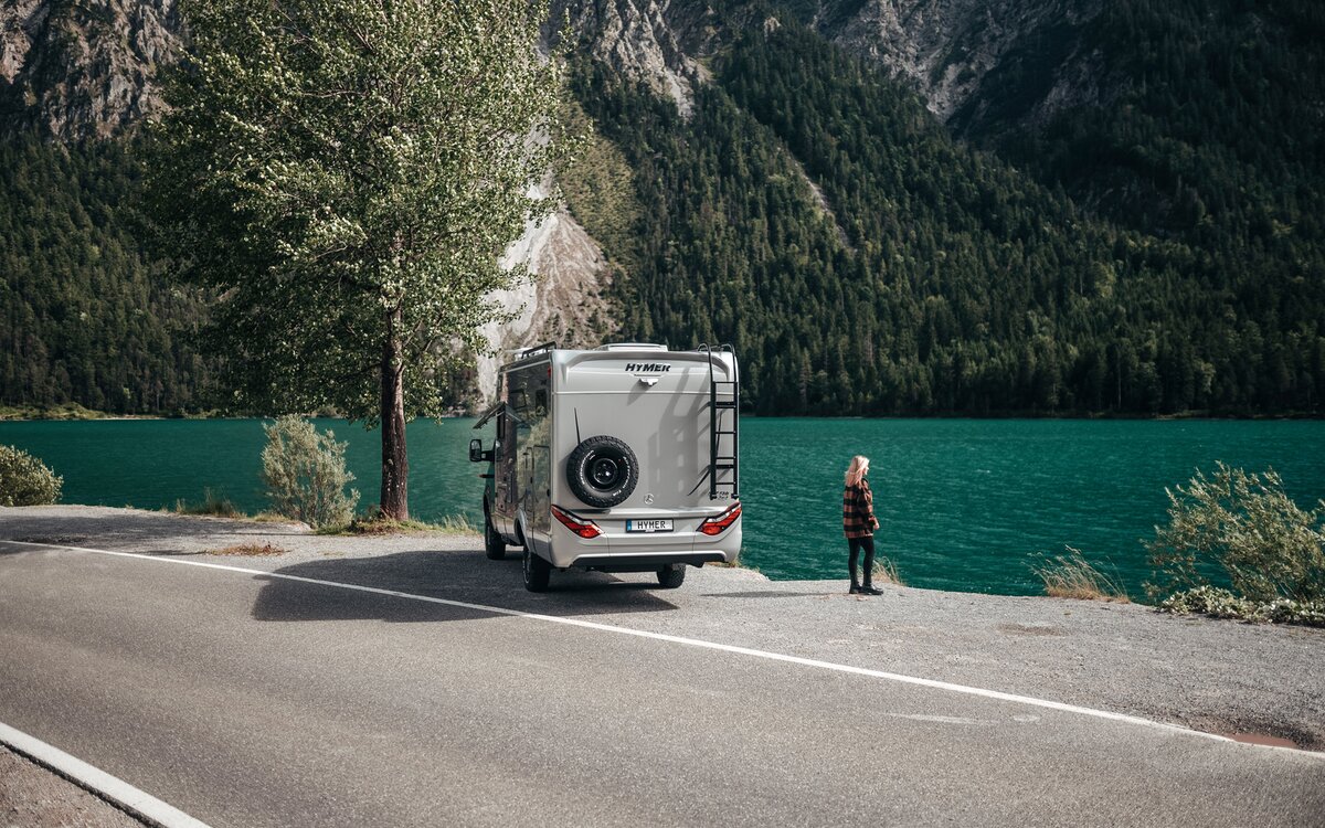 Eine Frau steht vor dem Heck des HYMER ML-T und blickt auf einen türkisfarbenen See.